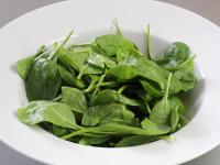 Place spinach leaves on a plate and drizzle with...